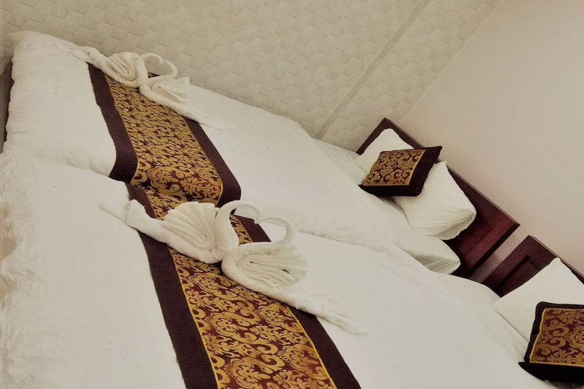 A neatly made bed with white linens, a decorative gold and brown bed runner, and matching pillows.