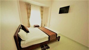 A bedroom with a bed, curtains, a small table, and a TV mounted on the wall. - Phuc Dang Huy Hotel (Xuan Huong - Da Lat)