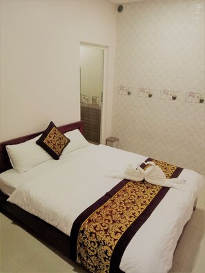 A hotel room with a bed, white linens, a decorative throw, and a wall with framed pictures.
