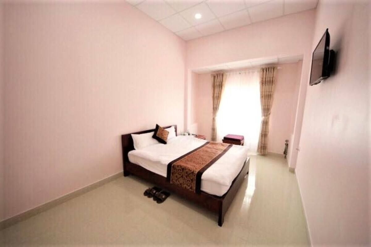 A bedroom with a bed, a TV mounted on the wall, and a window with curtains.