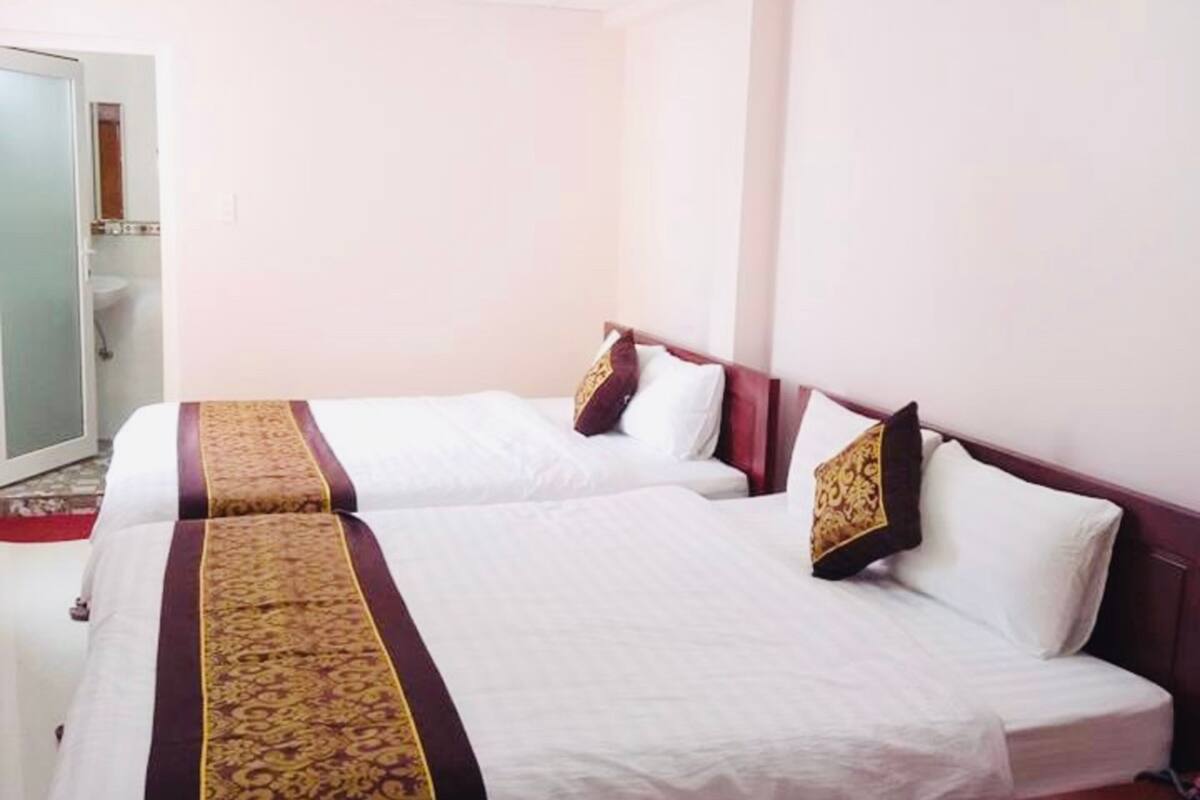 A hotel room with two beds, a wooden headboard, a nightstand, and a bathroom visible through an open door.