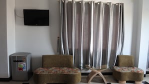 A room with two upholstered chairs with floral upholstery, a small table, a flat-screen TV mounted on the wall, and a refrigerator.