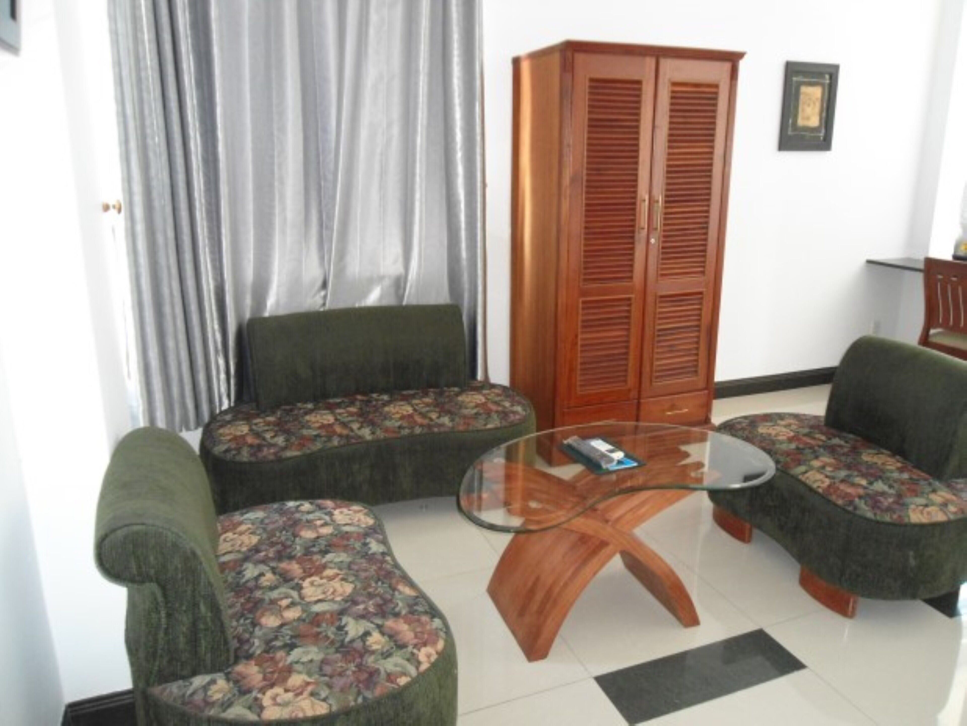 A living room with two green armchairs, a glass coffee table, and a wooden wardrobe.