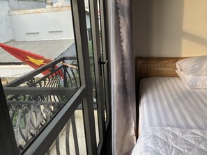 Una habitación con cama, ventana y vista a un balcón, además de una cortina.