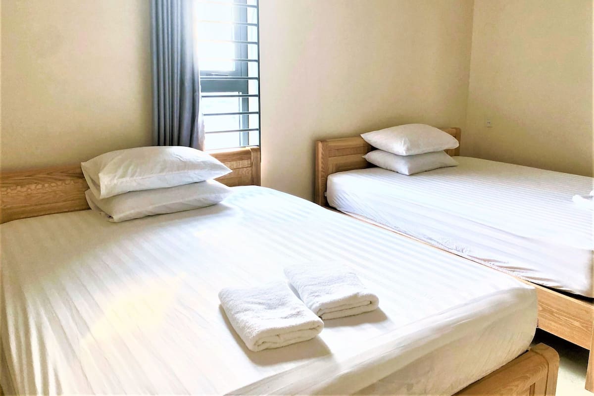 Two single beds with wooden headboards, white linens, and a window with blinds.