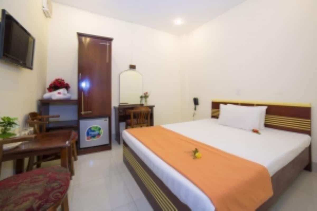 A hotel room with a bed, a desk, a chair, a television, and a refrigerator.