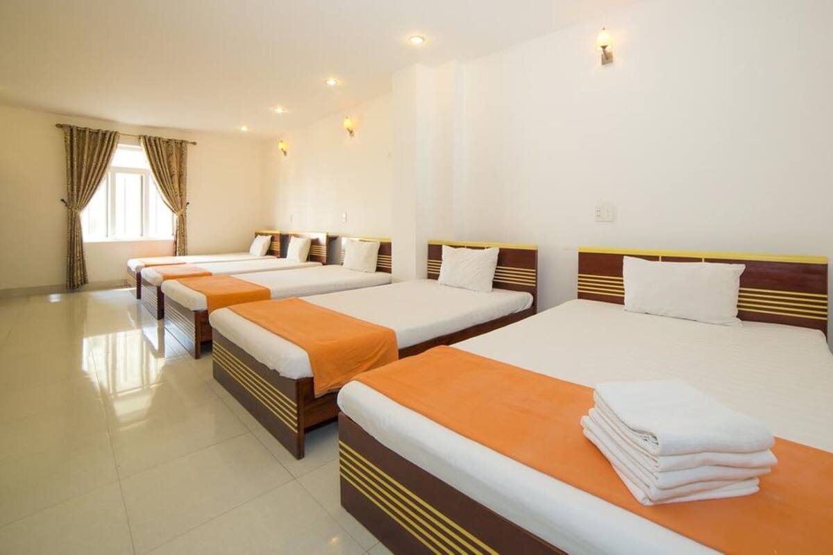 A hotel room with four single beds, each with an orange bedspread and white pillows.