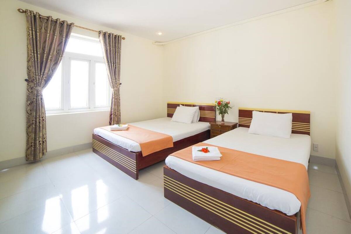 A hotel room with two beds, a window with curtains, and a nightstand with a vase of flowers.