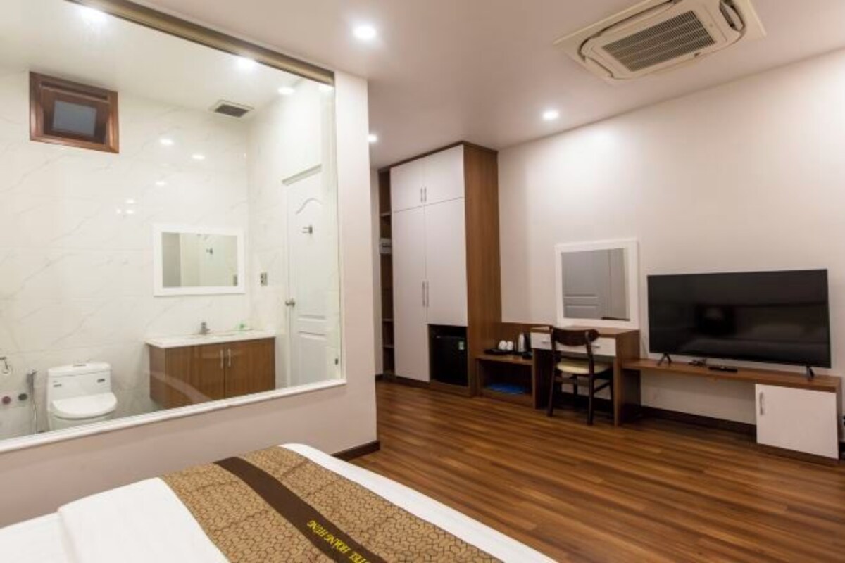 A modern hotel room with a large bed, a TV, a desk, and a wardrobe.