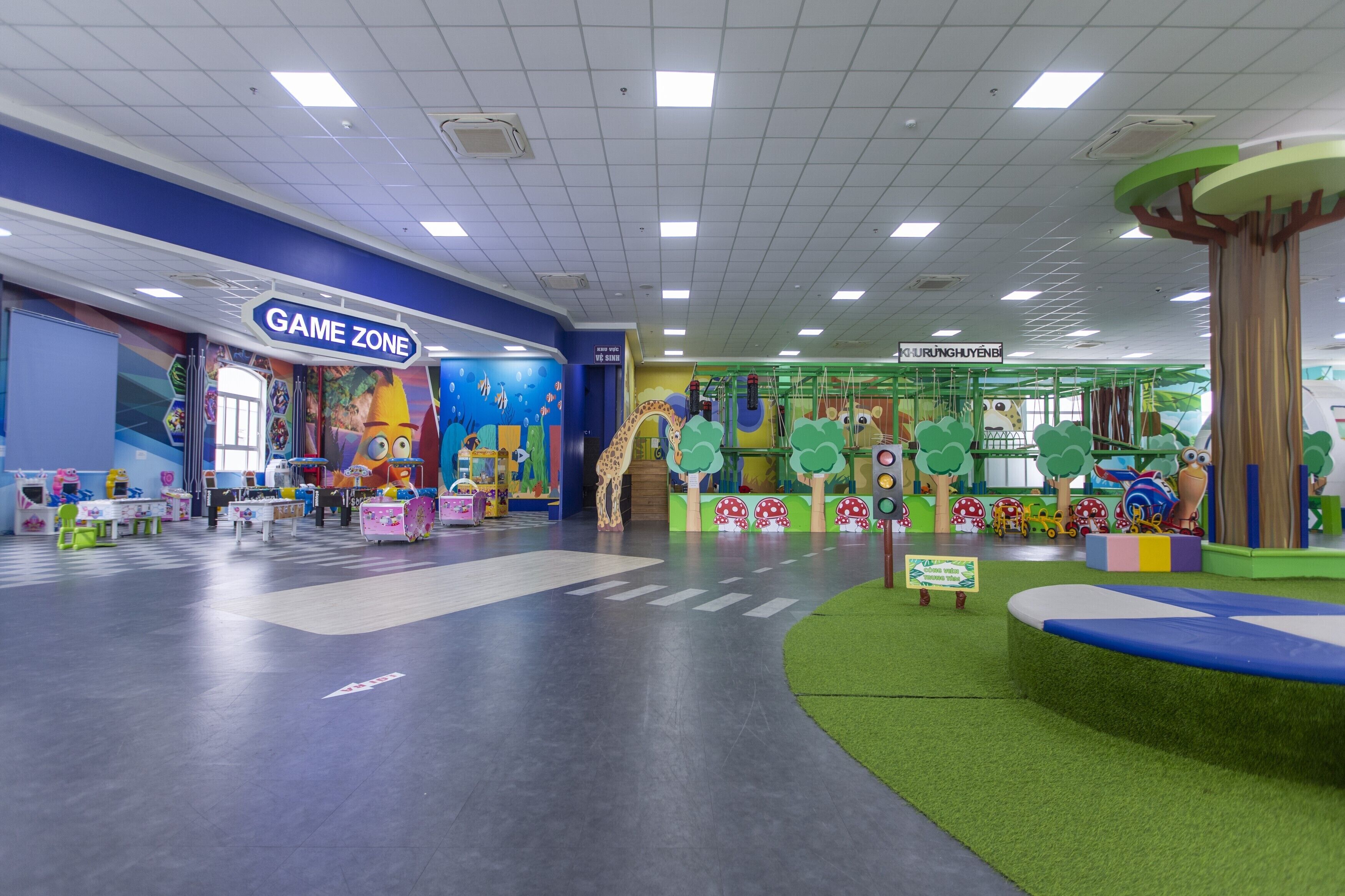 Ein Kinderspielbereich mit einem 'GAME ZONE'-Schild, Spielgeräten und einem grünen Teppichboden.