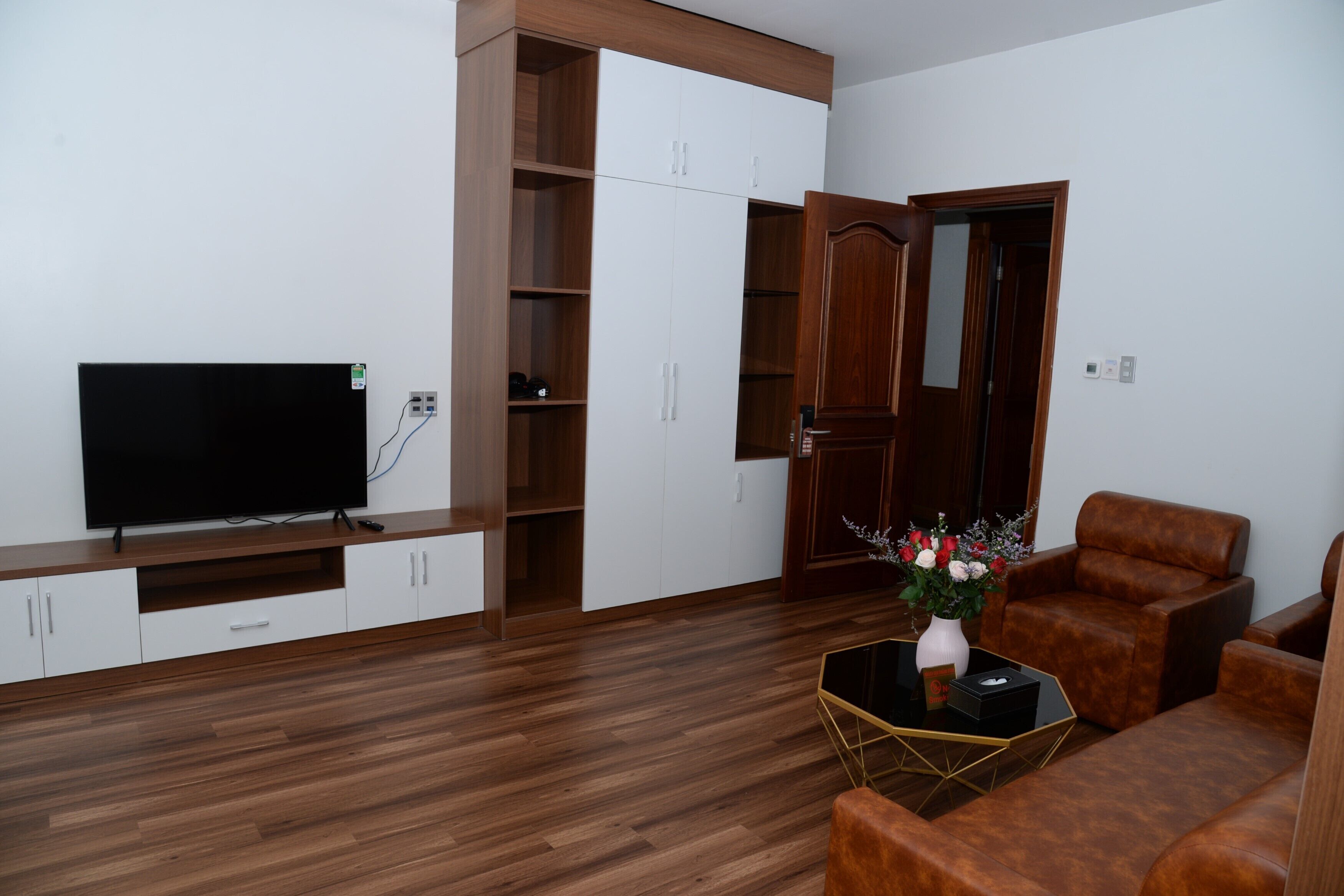 Una sala de estar con una televisión de pantalla plana, armarios de madera, un sofá y una mesita con un jarrón de flores.