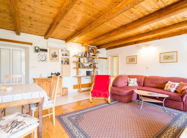 A cozy living room with a wooden ceiling, a red armchair, a sofa, a coffee table, and a bookshelf. - House Kocan (Konavle)