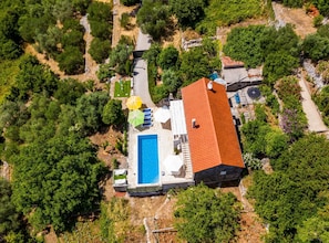 An aerial view of a property with a swimming pool, a red-roofed building, and surrounding greenery. - House Kocan (Konavle)