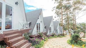 Une rangée de cabanes blanches, coiffées de toits triangulaires, avec des marches en bois menant à l’entrée, le tout entouré de verdure et bordé d’un chemin de pierres.