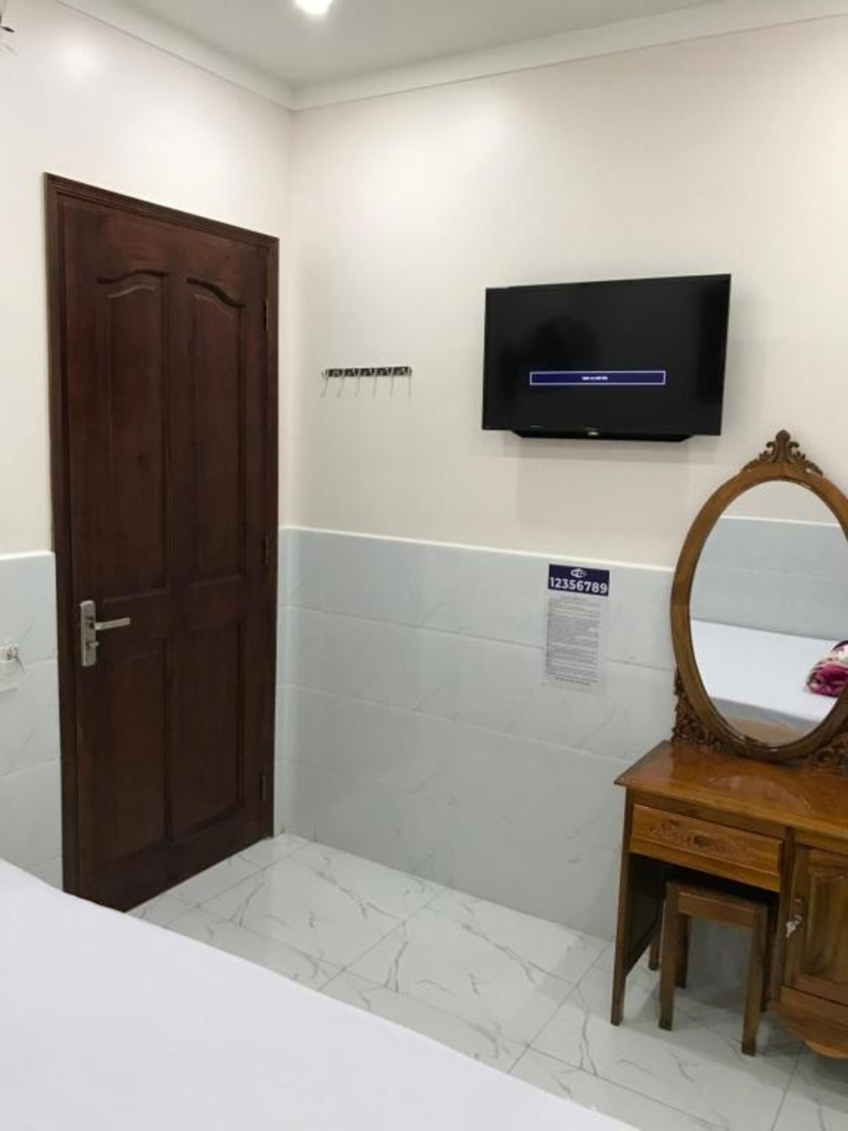 A bathroom with a wooden door, a vanity with a mirror, a wall-mounted TV, and a sign on the wall.