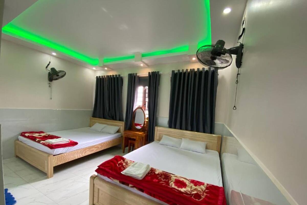 A hotel room with two single beds, a mirror, a wall-mounted fan, and green ceiling lights.