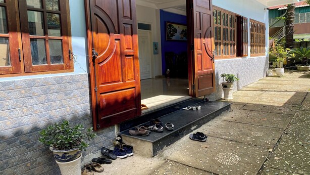Une entrée d’immeuble avec des portes en bois ouvertes, un mur recouvert de carreaux et une petite marche menant à un meuble à chaussures.