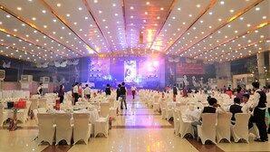 A banquet hall with round tables covered in white tablecloths and chairs, a stage with a large screen, and a ceiling with numerous lights. - Thang Loi Hotel (Ho Chi Minh City)