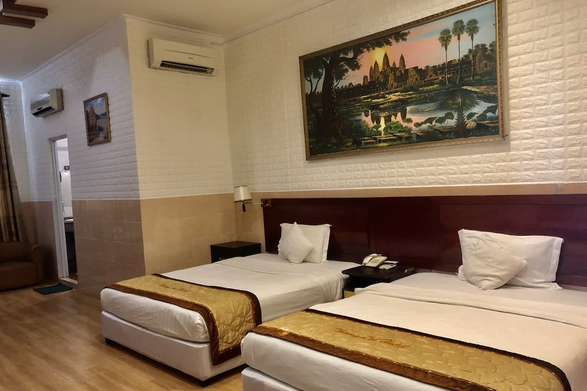 Une chambre d’hôtel avec deux lits, un tableau représentant un paysage et un plancher en bois.