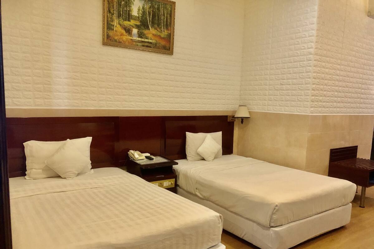 Une chambre d’hôtel avec deux lits, une tête de lit en bois, un tableau au mur et une table de chevet avec un téléphone.