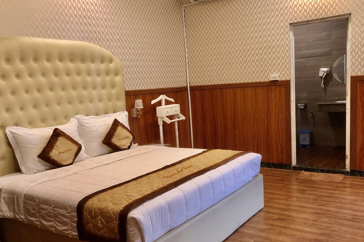 Un lit bien fait, avec une tête de lit capitonnée, une literie blanche et un coussin décoratif marron à motifs.