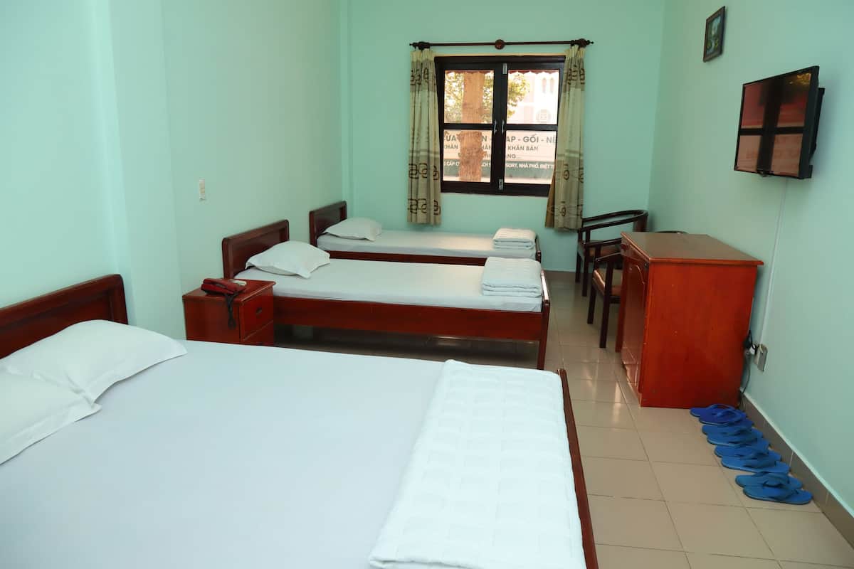Une chambre d’hôtel avec deux lits simples, un bureau en bois, une chaise, un téléviseur fixé au mur et une fenêtre avec des rideaux.