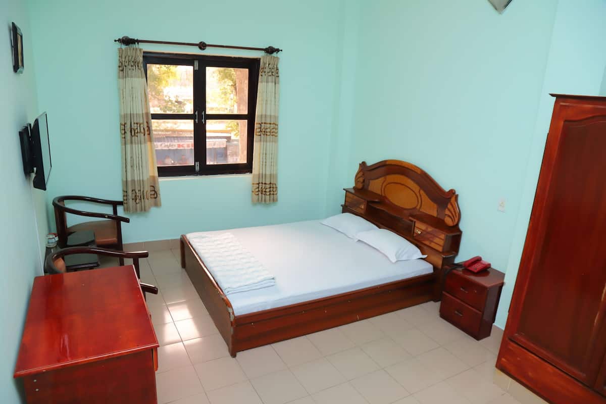 Une chambre à coucher avec un lit en bois, un bureau, une chaise, une armoire et une fenêtre avec des rideaux.