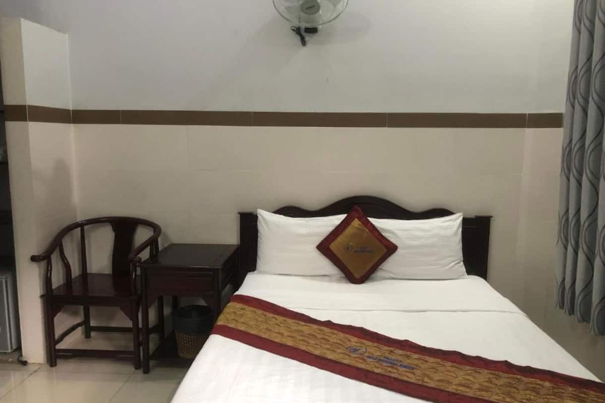 Ein Hotelzimmer mit einem Bett, einem Holzstuhl, einem kleinen Tisch und einem Wandventilator.