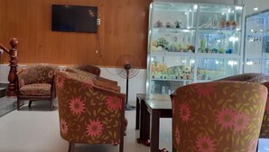 A room with floral-patterned chairs, a wooden staircase, a television mounted on the wall, and a glass display case with various items. - Nguyen Hotel and Homestay (Da Nang)
