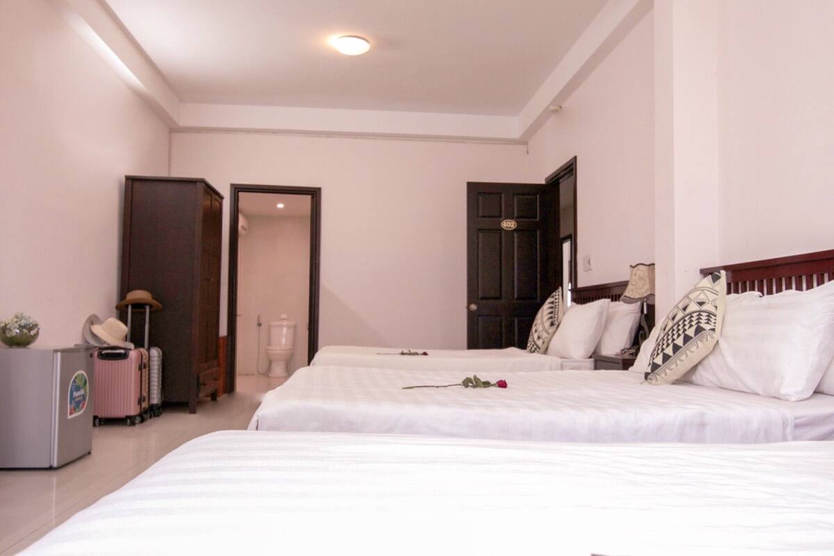 A hotel room with two beds, a desk with a computer, a suitcase, and a small refrigerator.