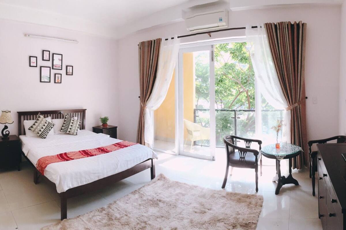 A bedroom with a bed, a TV, a desk, and a balcony with curtains.