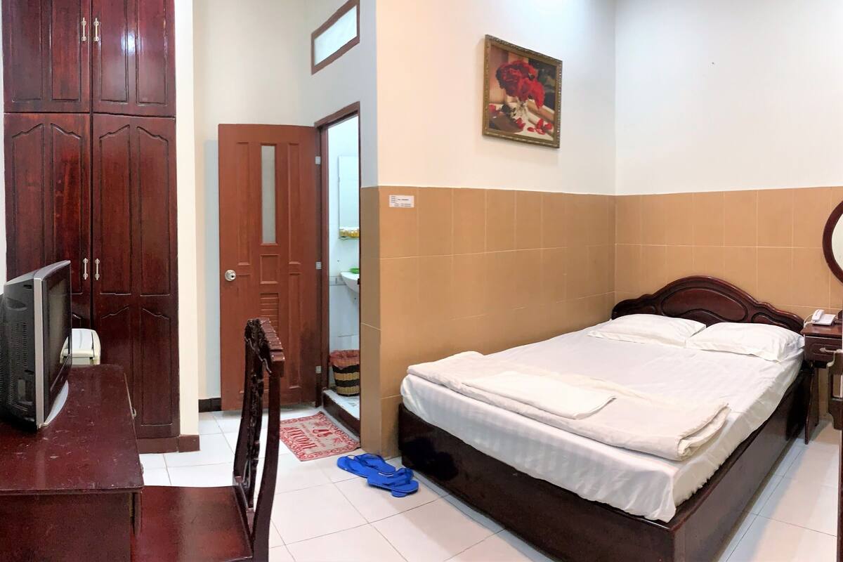 Une chambre d’hôtel avec un lit, un bureau doté d’une télévision, une armoire et une salle de bain visible à travers une porte ouverte.
