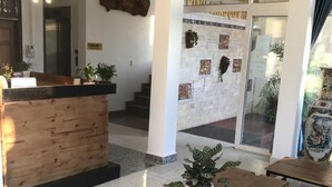 A reception area with a wooden desk, potted plants, and a stone wall with artwork. - Thao Trang Hotel Dong Hoi (Dong Hoi)