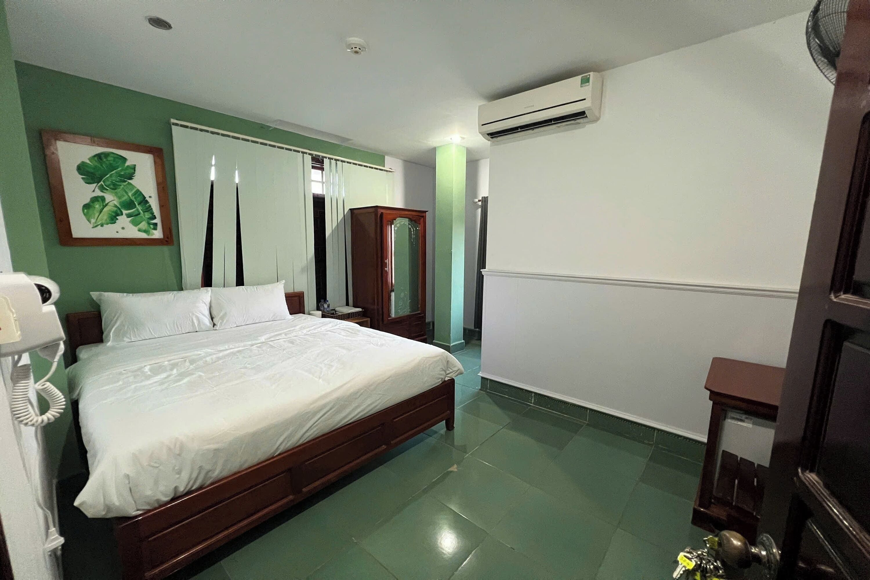 A bedroom with a bed, a bedside telephone, a mirror, and a wardrobe.