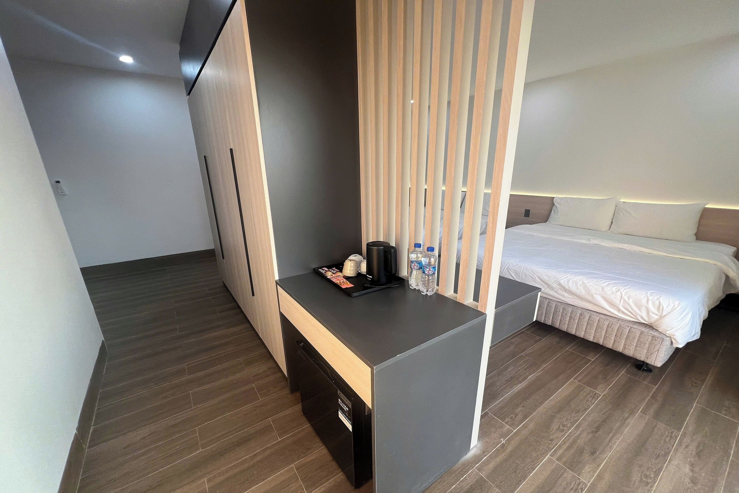 A modern hotel room with a bed, a small desk with a coffee maker, and a water bottle.