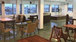A spacious indoor area with multiple tables and chairs, large windows offering views of the city, and a fan on the floor. - Thao Trang Hotel Dong Hoi (Dong Hoi)