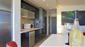 A modern kitchen with a microwave, knives, and a wine bottle on the counter.