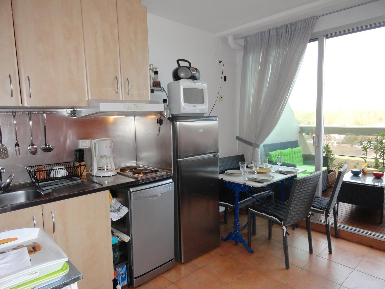 Et kompakt køkken med køleskab, komfur, mikrobølgeovn og et lille spiseområde med bord og stole.