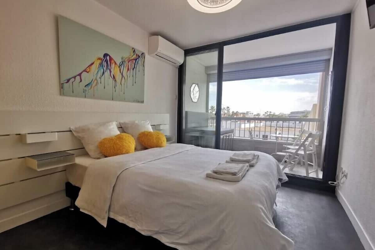 Une chambre d’hôtel moderne avec un grand lit, un tableau au mur et un balcon avec des chaises.