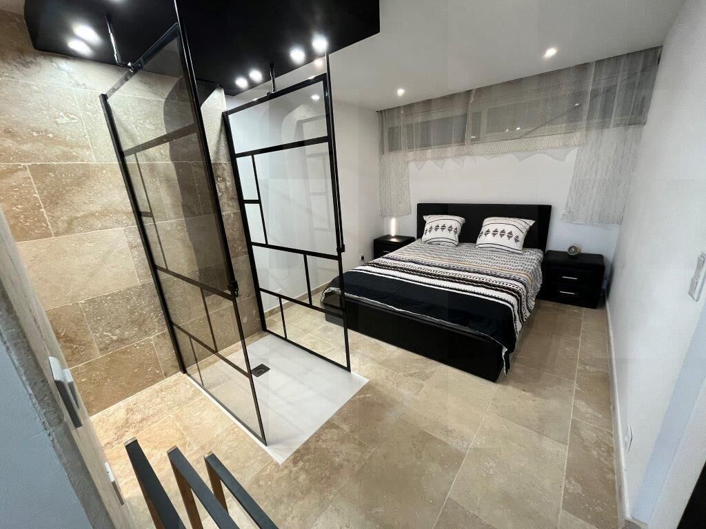 A modern bedroom with a large bed, a glass partition, and a nightstand.