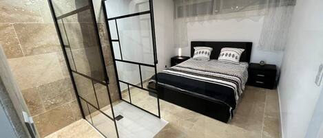 A modern bedroom with a large bed, a glass partition, and a nightstand.
