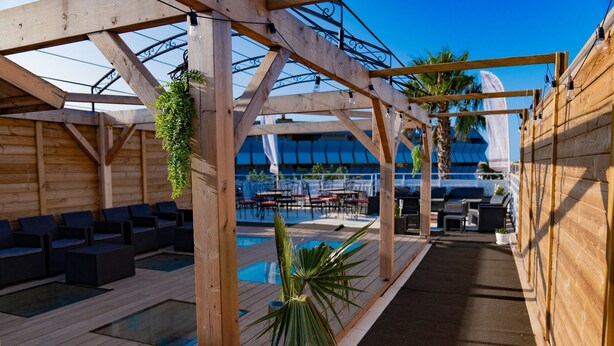 A rooftop pool area with wooden pergolas, seating, and potted plants.