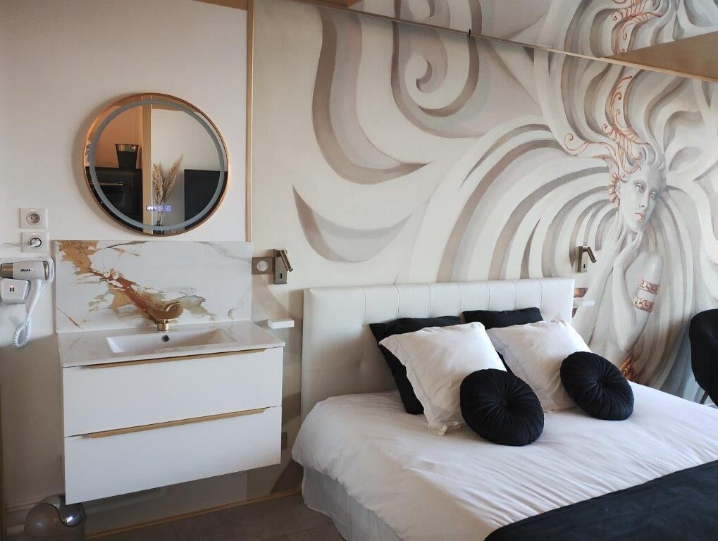 Un dormitorio moderno con una cama blanca, almohadas negras y blancas, un espejo redondo y un mural decorativo en la pared.