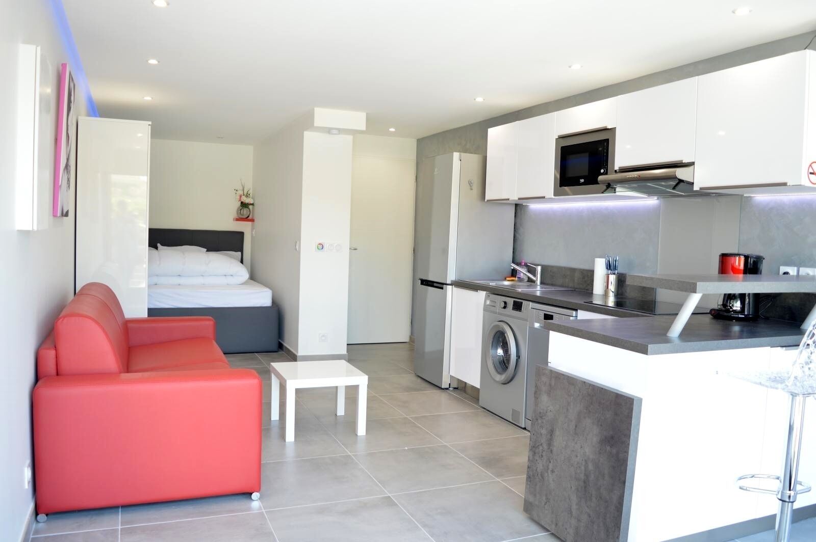 Un apartamento moderno con kitchenette, lavadora, cama y sofá rojo.
