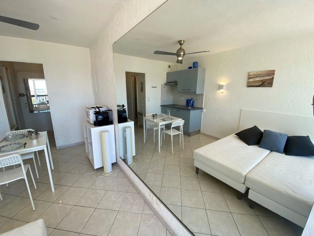 A compact hotel room with a bed, a small kitchenette, a dining area, and a ceiling fan.