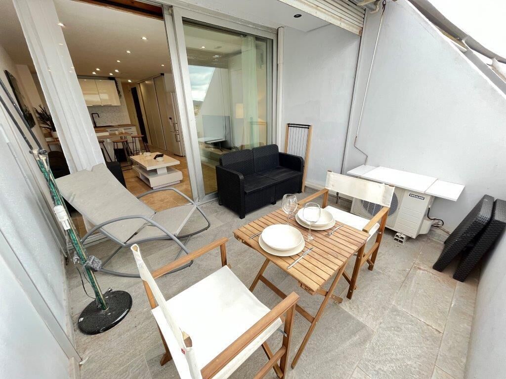 A modern living space with a wooden dining table set for two, a black sofa, and a glass door leading to a kitchen.