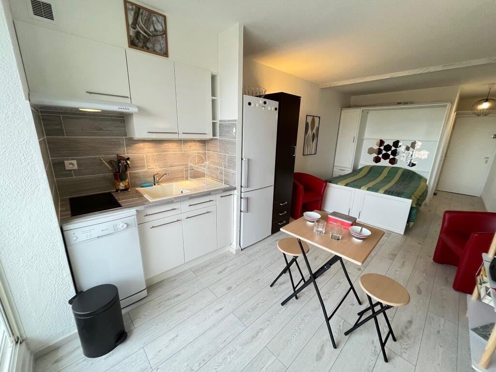 A compact kitchen with white cabinets, a dishwasher, and a small dining area with two stools.