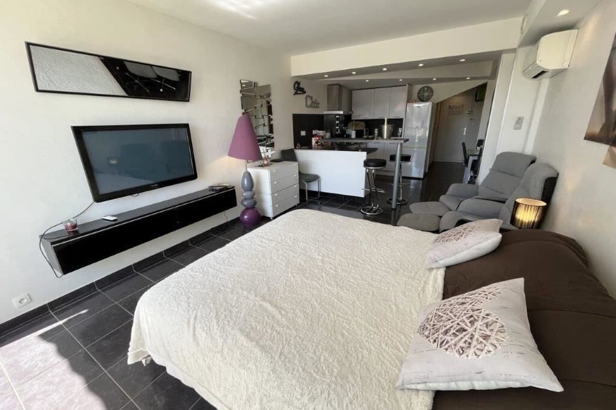 Une chambre moderne avec un grand lit, une télévision, un bureau et, au fond, un coin cuisine.