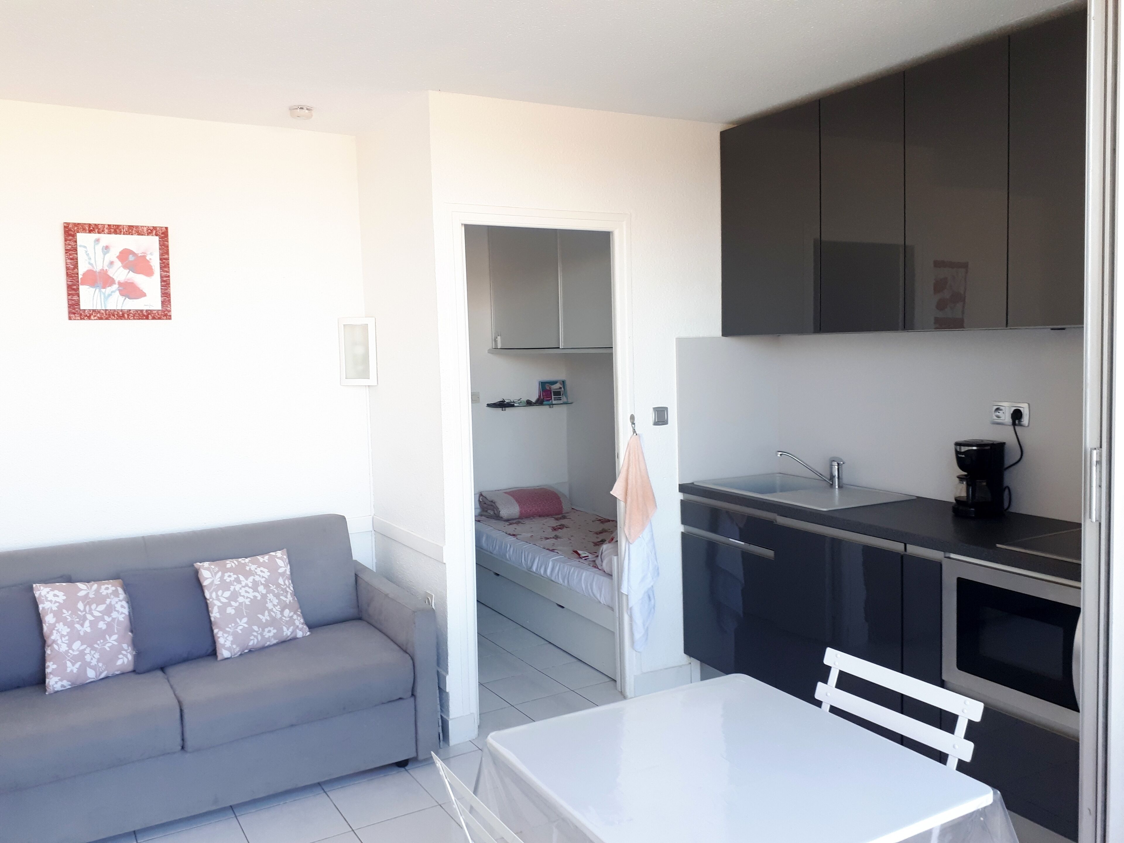 Un espace de vie compact comprenant un coin cuisine, un canapé, une petite table à manger et un lit à l’arrière-plan.