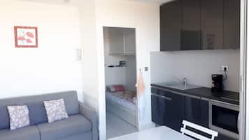A compact living space with a kitchenette, a sofa, a small dining table, and a bed in the background.